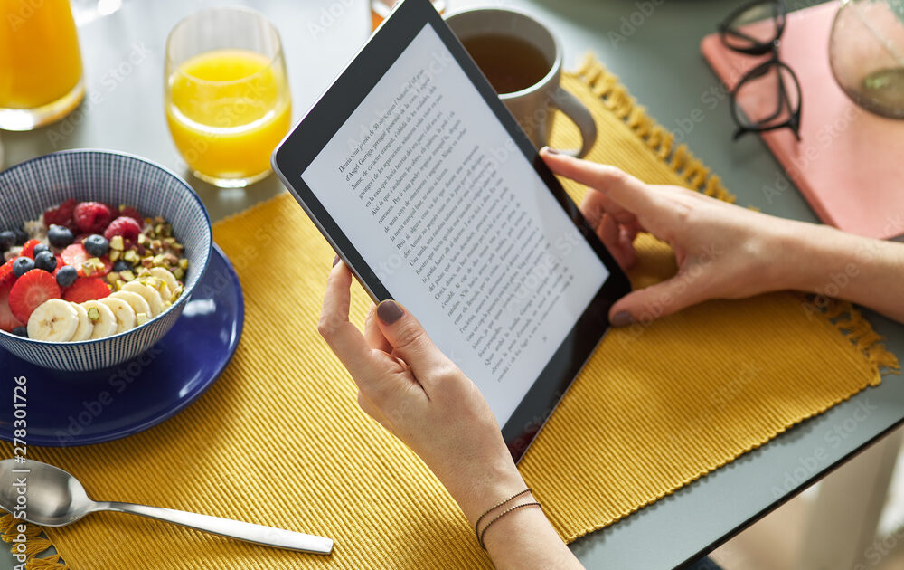 Woman reading ebook via tablet while having breakfast at home.