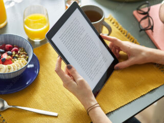 Woman reading ebook via tablet while having breakfast at home.
