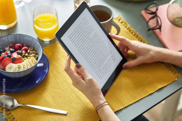 Woman reading ebook via tablet while having breakfast at home.